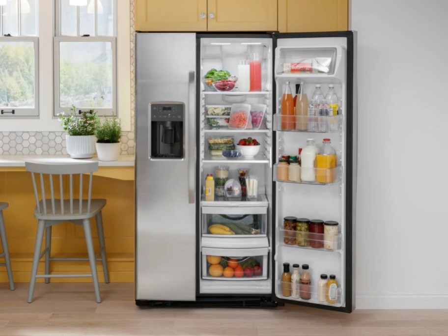 a stainless steel side by side fridge in a kitchen with 1 door open showing the food and drinks inside