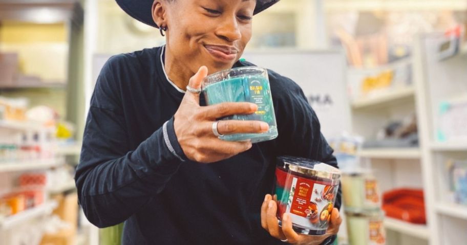 Woman holding two candles and smelling one of them.