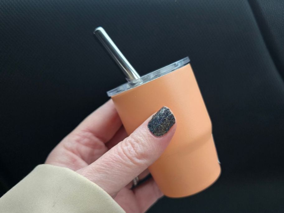 A person holding a tiny orange tumbler