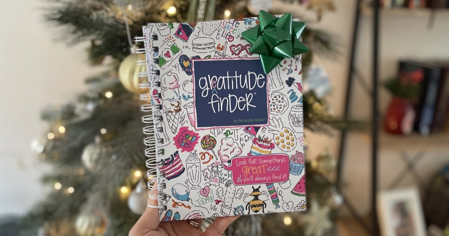 hand holding gratitude journal in front of christmas tree