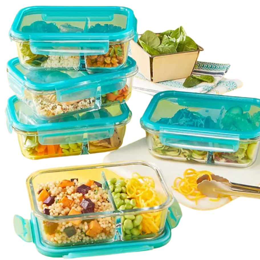 a set of glass divided food containers with green lids, all have food in them