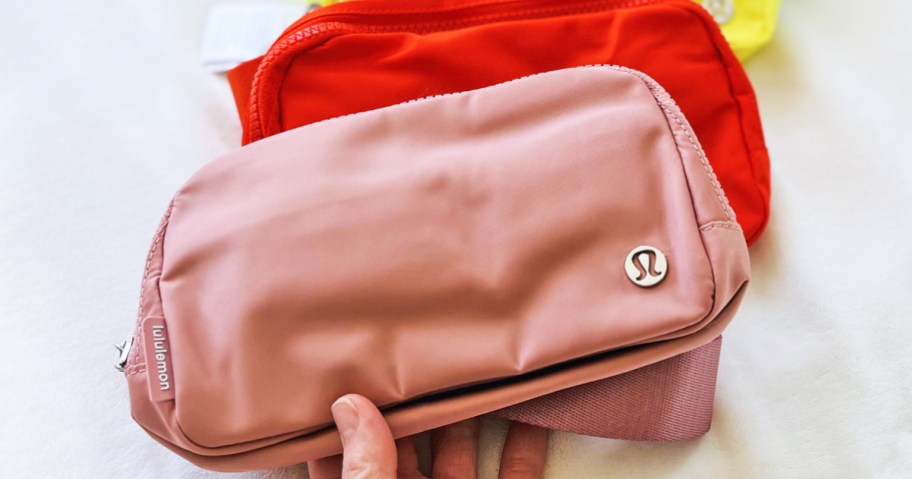 hand holding up pink and red lululemon belt bags