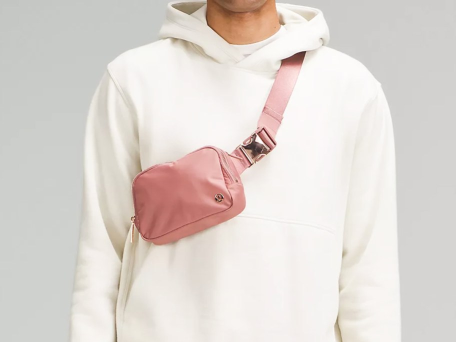 person in a white hoodie with a pink belt bag across chest 