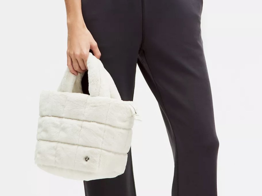 woman in dark grey pants holding a white fleece tote bag