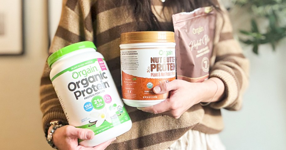 woman holding three containers of Orgain protein powders