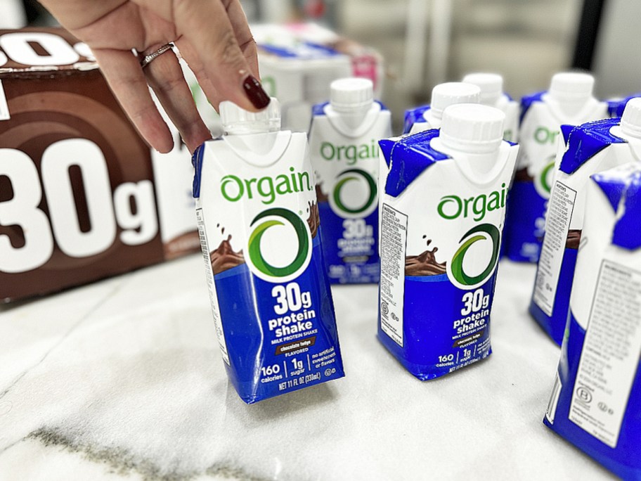 a hand reaching for a ready to drink Orgain shake bottle with many more bottles near it