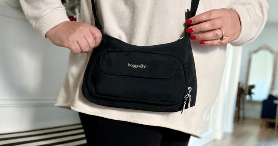 woman with a black Baggallini crossbody bag on, she's also wearing a cream sweater and black pants