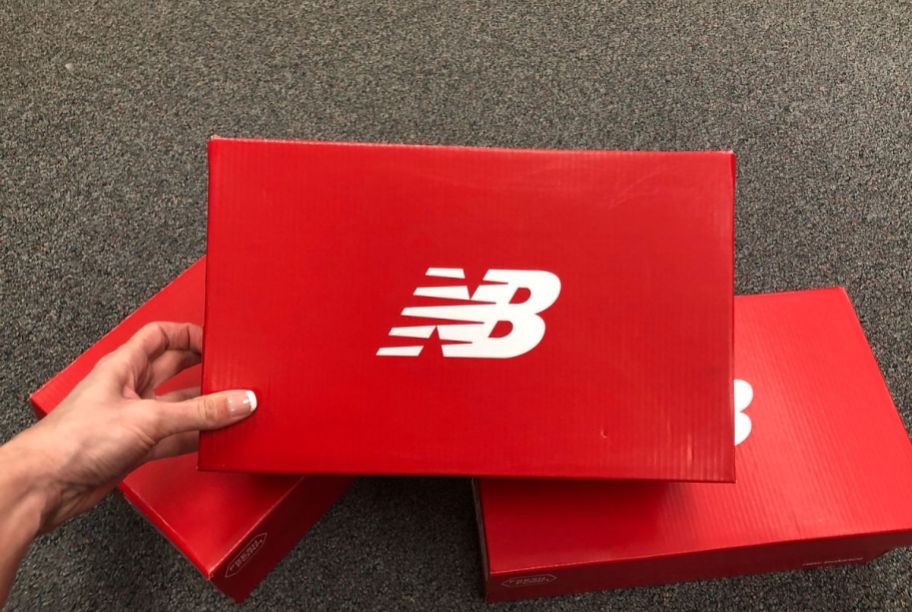 a womans hand reaching for a red new balance shoe box.