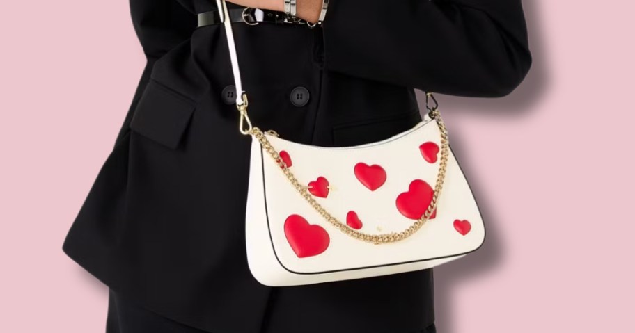 woman wearing a black dress with a cream color crossbody bag that has red hearts on it