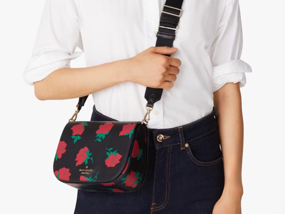 woman wearing a white button down shirt and black jeans with a black crossbody bag that has red roses printed on it