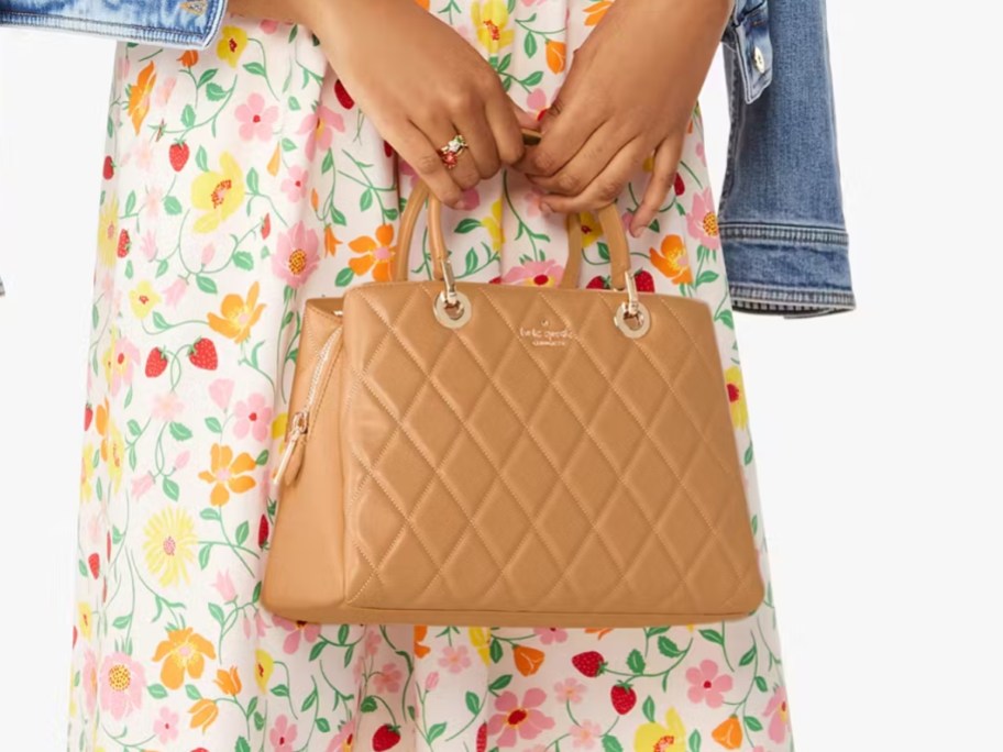 image of woman holding a tan quilted purse, she's wearing a floral skirt