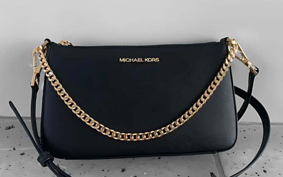 a medium black leather crossbody handbag with a gold chain strap sitting on the floor