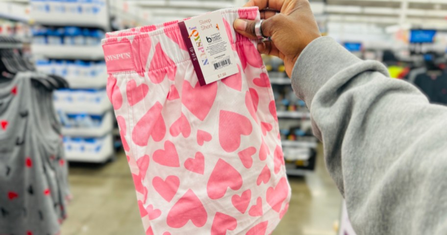 Woman holding up pink and white heart boxer sleep shorts inside Walmart store