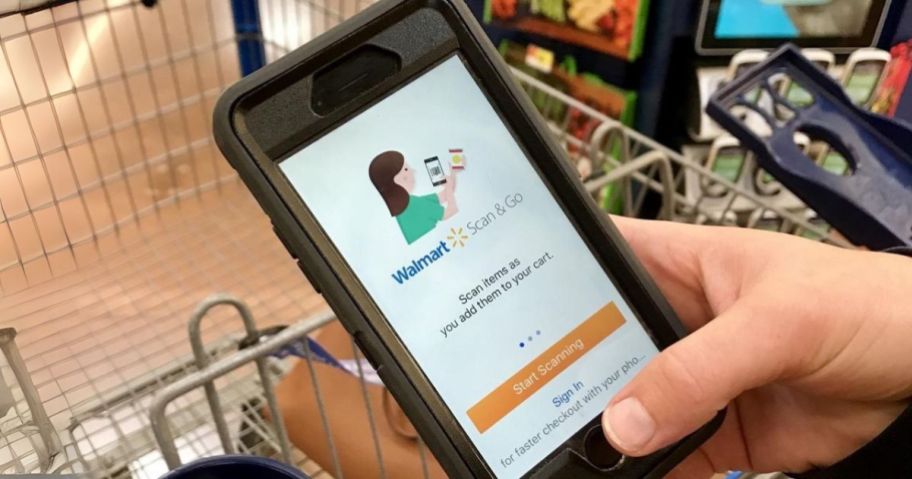 hand holding phone with walmart scan and go on it in store over shopping cart