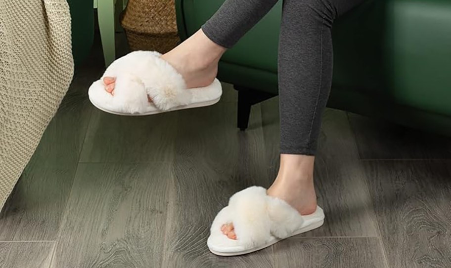 woman sitting on sofa wearing a white pair of parlovable fuzzy slippers