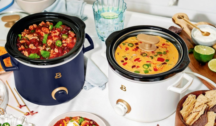 a navy slow cooker full of chili next to a white slow cooker full of queso