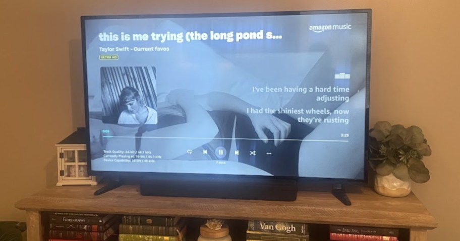 a large TV with a soundbar in front on a TV stand playing Taylor Swift thru the Amazon Music TV app