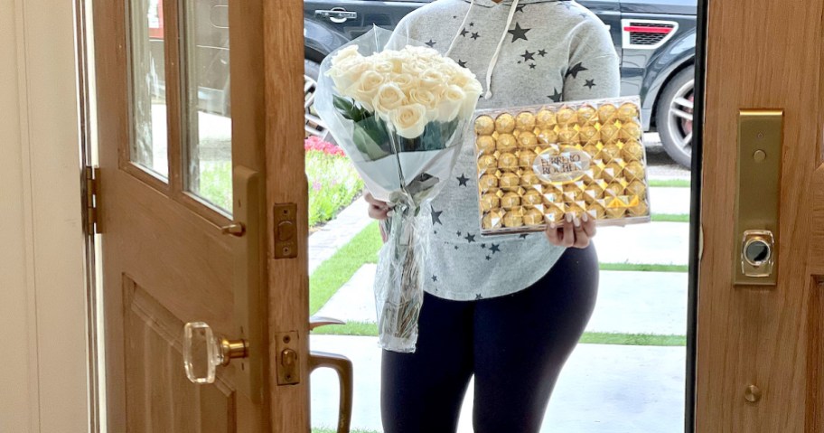 woman holding flowers and chocolates in front of door