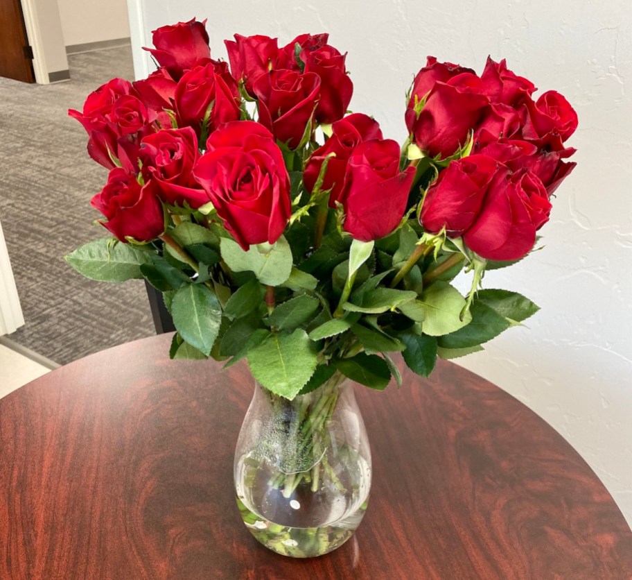 red roses in clear glass vase on wood table