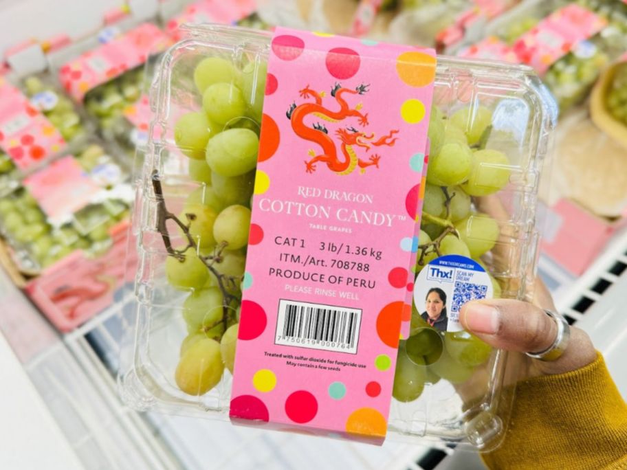 a womans hand holding a container of cotton candy grapes