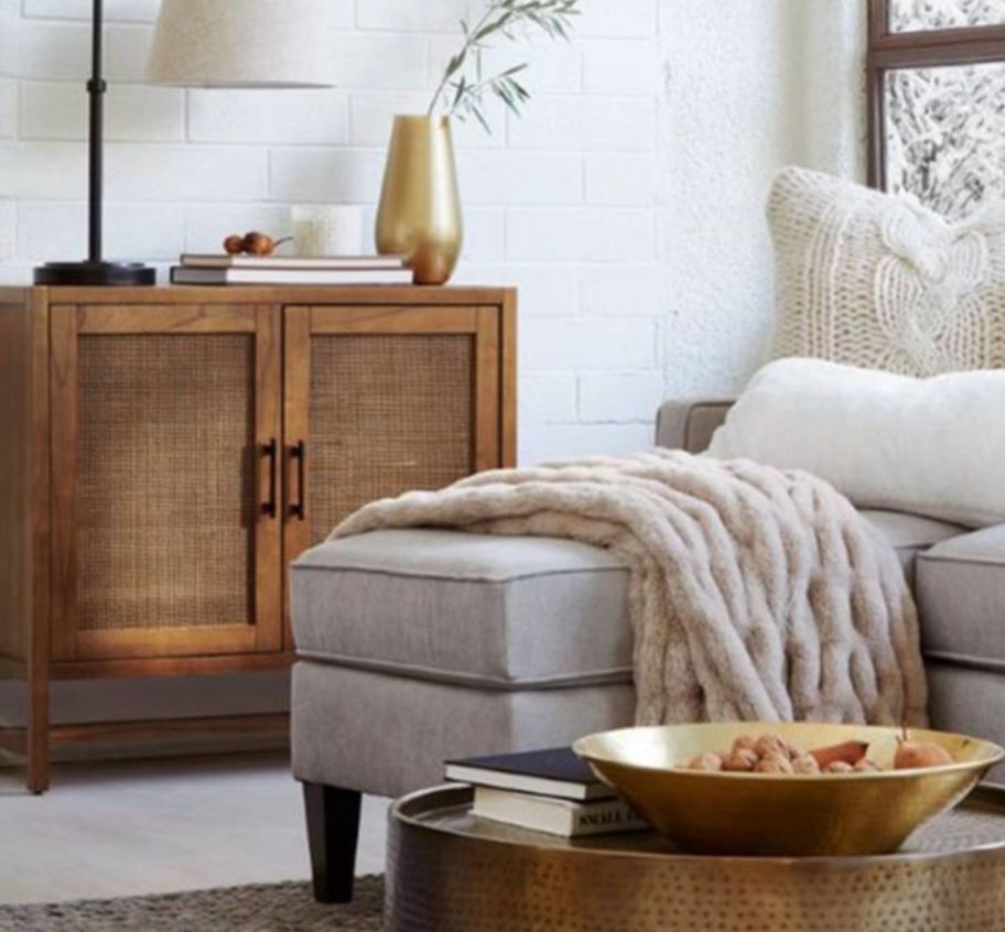 a two door wicker cabinet in a living room pictured with a sectional and cocktail table.