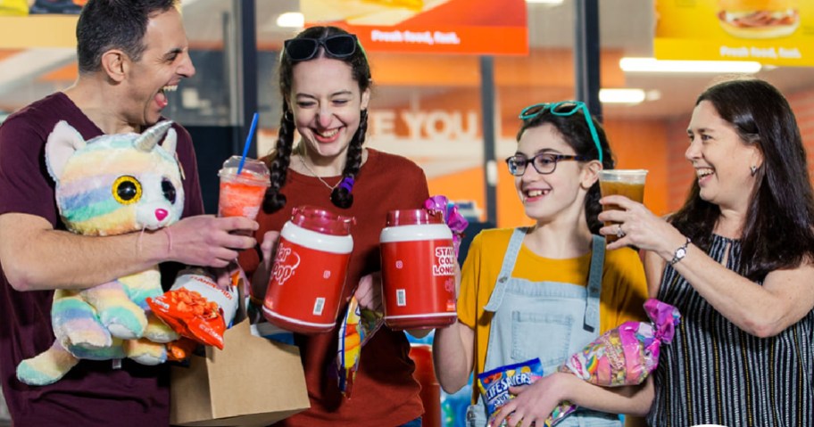 family standing in front of convenience store holding stuffed animal, drinks and snacks