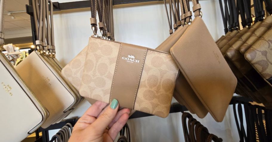 A woman holding a Corner Zip Wristlet In Signature Canvas in the store