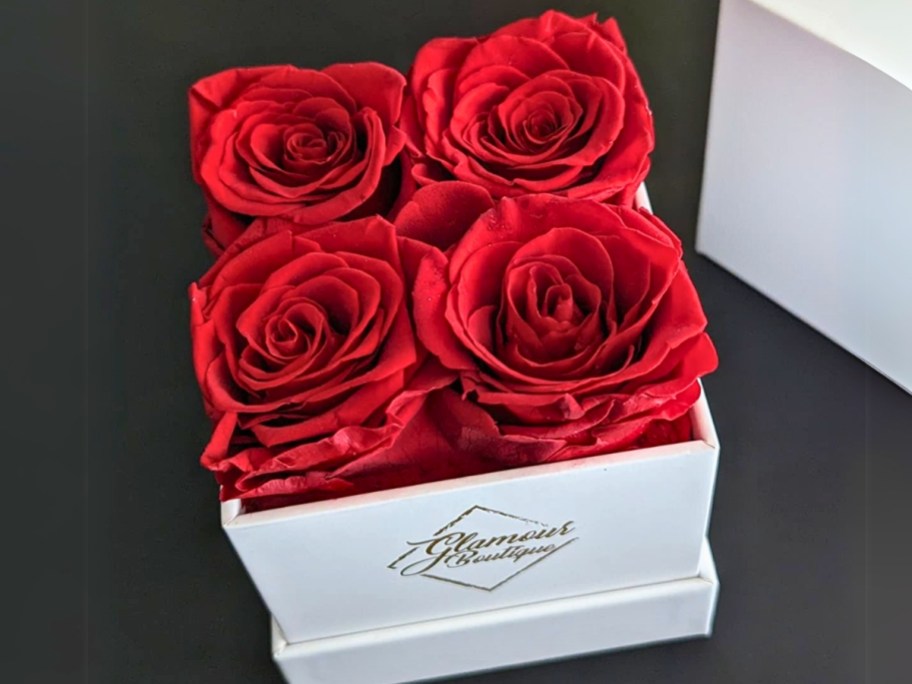 a white box with gold lettering with 4 red roses in it sitting on a table