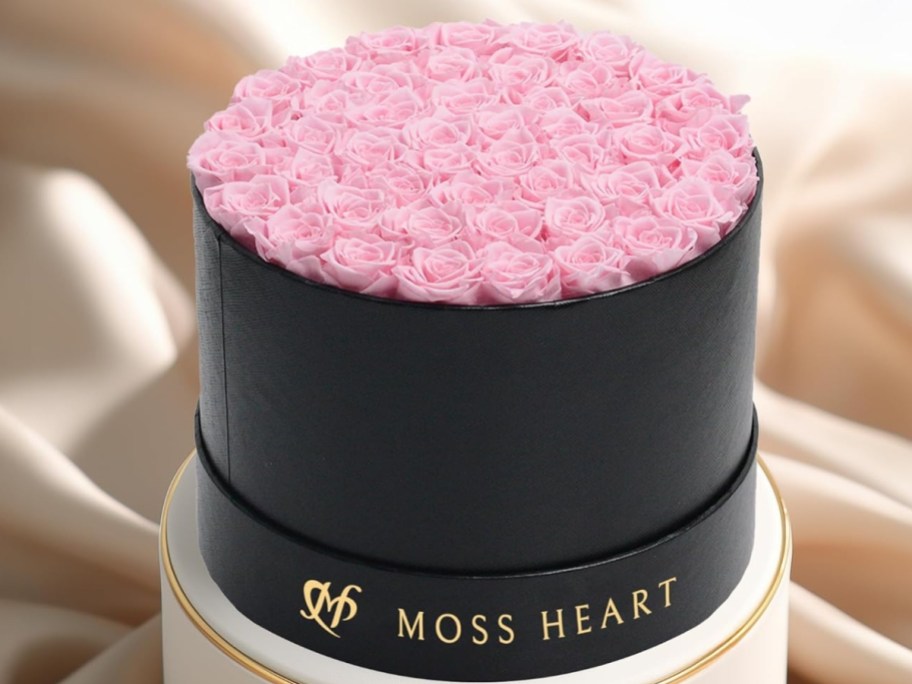 a large round black box with gold lettering filled with light pink roses