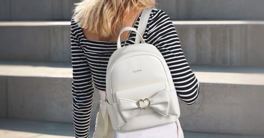 woman walking up cement steps - she's wearing a <a href='https://www.chiseza.com/dr-martens-mens-black-leather-moccasin-boots' target='_blank' rel='follow'>black</a> and white stripe top and white pants and carrying a and carrying a white mini backpack purse that has a bow and silver heart accent on it” width=”912″ height=”479″></p>
<p>Through February 9th, head on over to <a href=