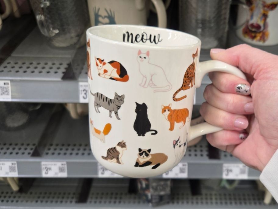 A person holding a mug with cats on it 