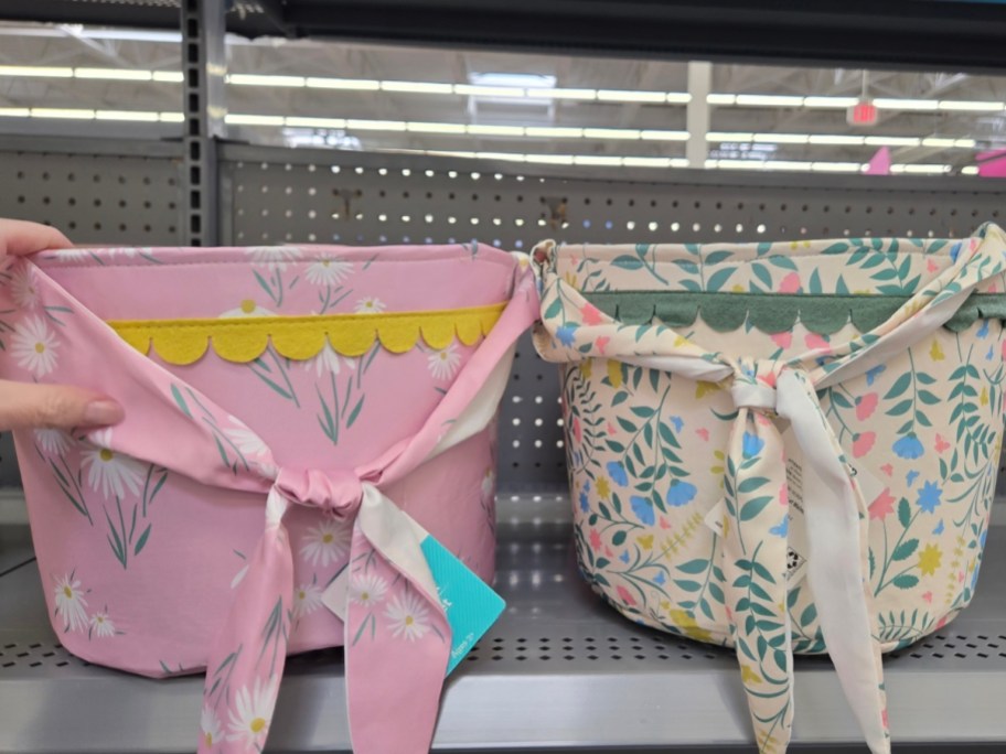 hand reaching for a pink floral fabric Easter basket on a store shelf, a white floral basket sits next to it