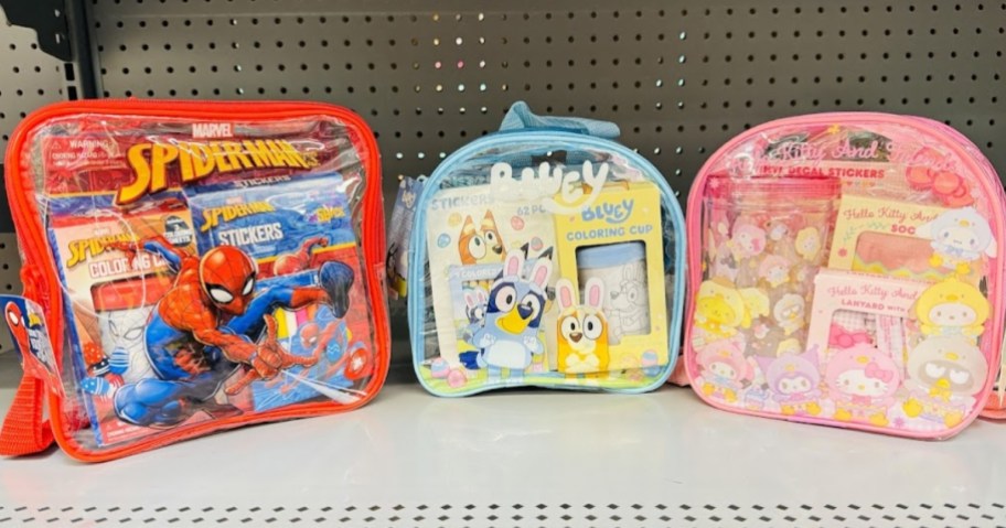 a Spiderman, a Bluey, and a Hello Kitty backpack with a water bottle, activity books, and stickers on a store shelf