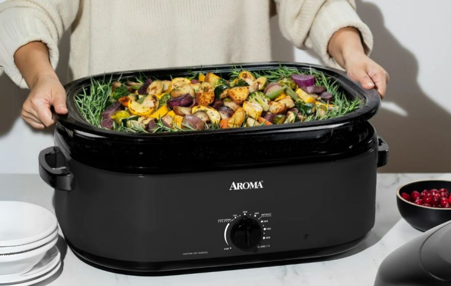 a woman lifiting the pan out of an 18-quart electric roaster 