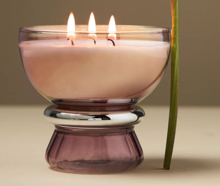 a large 3 wick candle in a violet glass bowl