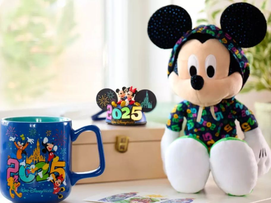 A Micket Mouse Hat Ornament on a book between a large mug and a mickey plush