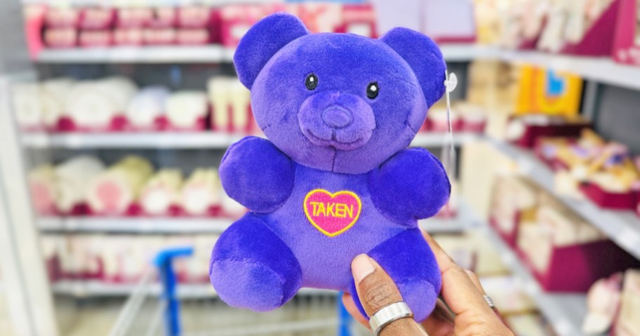 hand holding up a small purple gummy bear plush with a heart that says taken