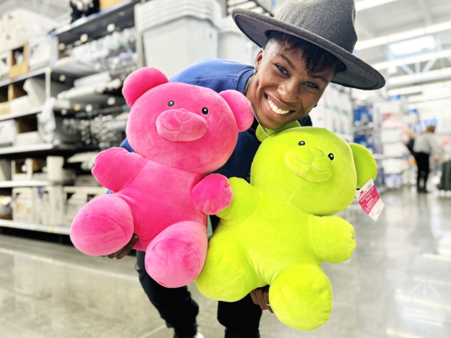 woman holding up pink and green gummy bear plushies in store