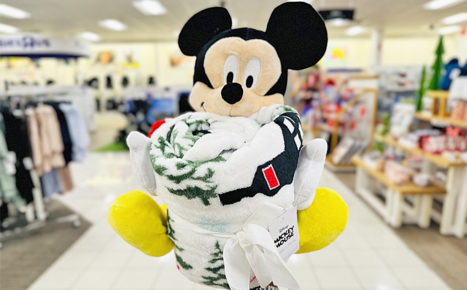 hand holding up a Mickey Mouse plush and throw blanket set in store