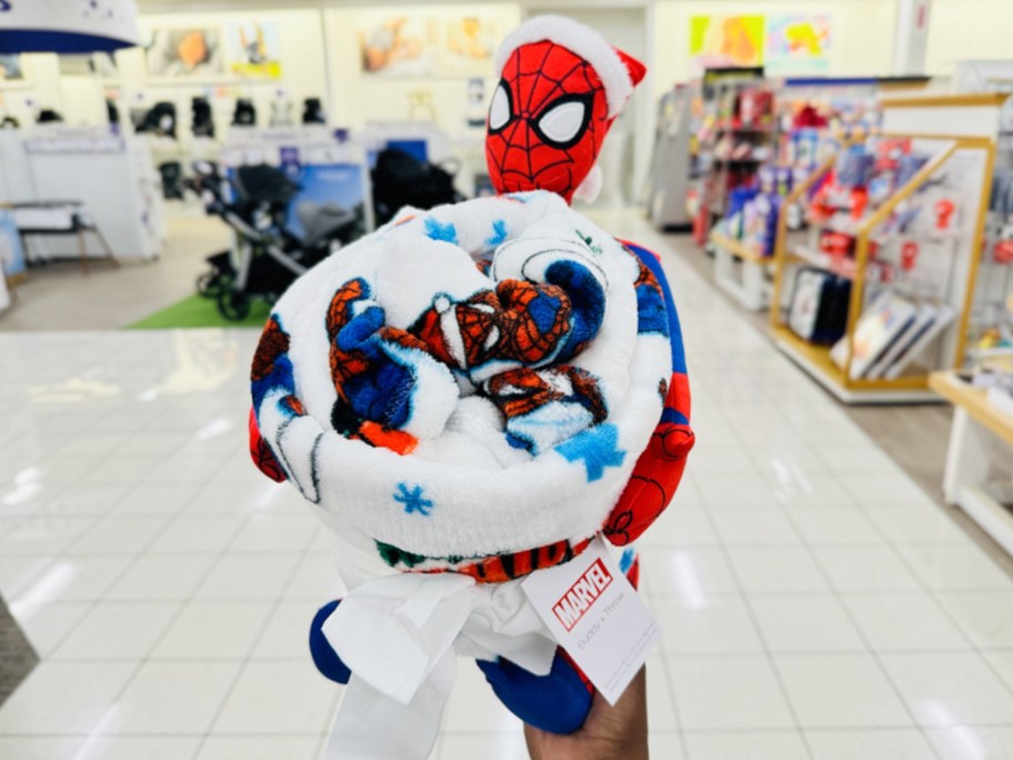 hand holding up a Spiderman plush and throw blanket set in store