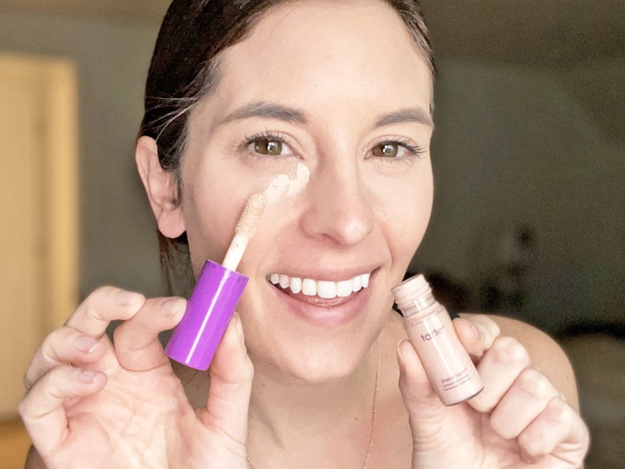 woman applying small tube of tarte shape tape concealer under her eyes