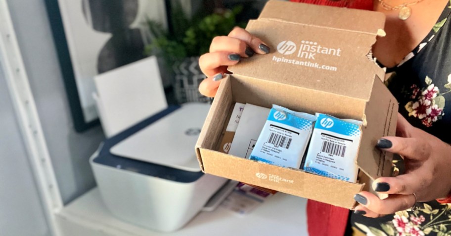 a woman stands next to HP printer holding instant ink box.