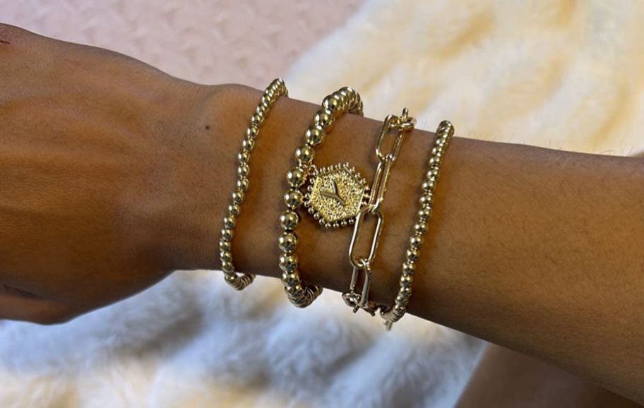 a woman's wrist shown wearing a four piece gold inital bracelet set 