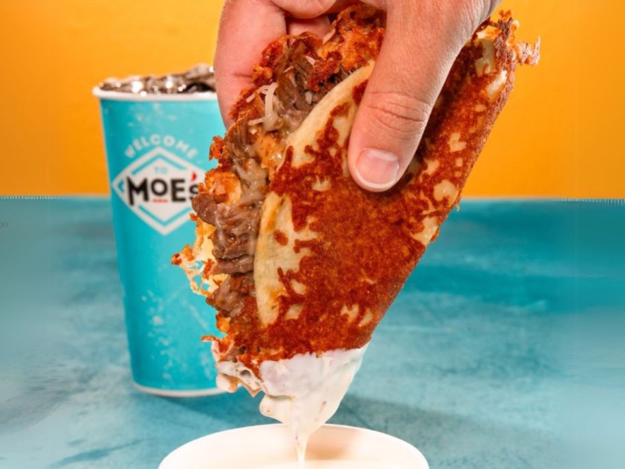 hand dipping moe's Quesabirria Taco in queso