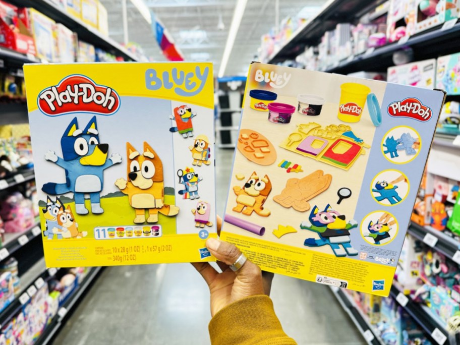 holding up two <a href='https://sjf.a8c.myftpupload.com/product/crown-signature-collection' target='_blank' rel='follow'>boxes</a> of Play-Doh Bluey Make ‘n Mash Costumes Playsets in store” width=”912″ height=”684″></p>
<p>This set includes Bluey and Bingo shaped stamps plus stamps to dress them in swimsuits, princess costumes, silly granny blankets, and more. Plus it includes 11 cans of Play-Doh in various colors.</p>
<p class=