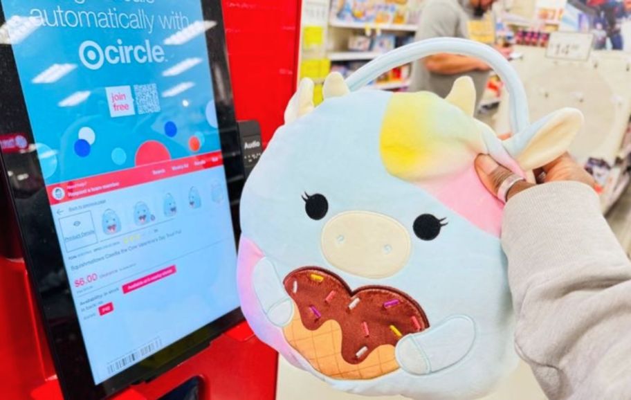 womans hand holding a squishmallow basket next to a price scanner