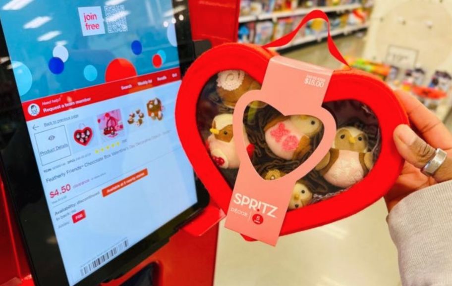 womans hand holding a red heart shaped box of felt birds next to a price scanner