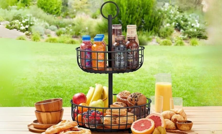 a black iron 2 tier stand filled with snacks drinks and fresh fruit