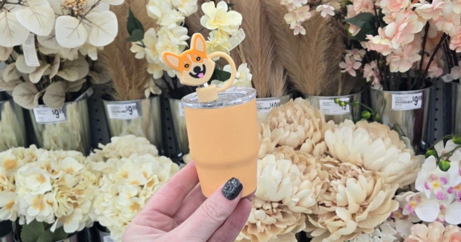 hand holding a peach color mini tumbler that has a silicone straw topper that looks like a Corgi dog