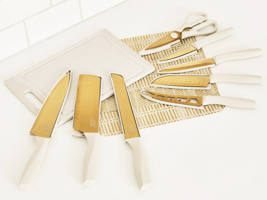 a set of white and gold knives, kitchen sheers, cutting board and cutting mats on a counter